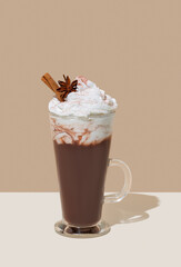 Hot chocolate with whipped cream, cinnamon and spices in a tall glass on a white and beige background