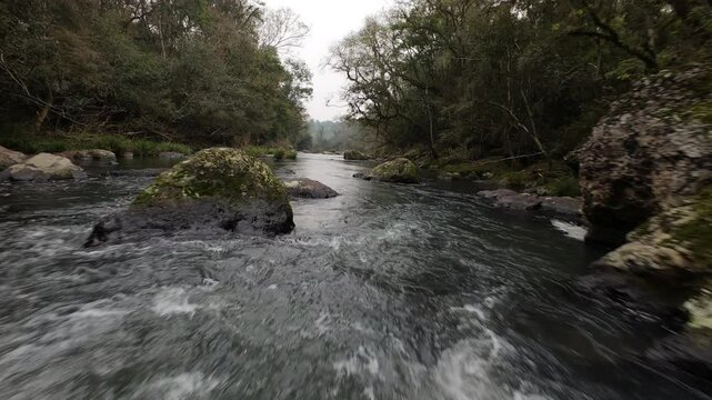 River flowing through a rocky landscape in Misiones, Argentina, showcasing the natural beauty of Gruta India with lush vegetation and dynamic water movement, FPV drone footage