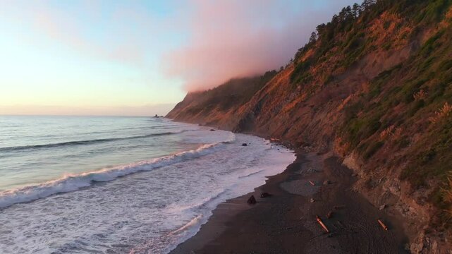 Northern California waves crashing bluffs cliffside mountain rocky rugged remote coast aerial drone vibrant sunset USAL Beach Campground Sinkyone Wilderness surf swell black sand forward down motion