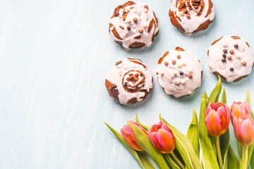 Cupcakes or muffins with icing and tulips on a light blue background. Easter cakes with chocolate chips. Space for text. View from above. Flat lay.