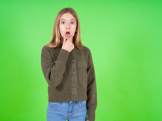 beautiful teen girl wearing green sweater Looking fascinated with disbelief, surprise and amazed expression with hands on chin
