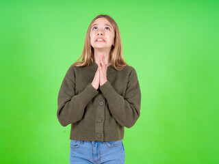 beautiful teen girl wearing green sweater begging and praying with hands together with hope...