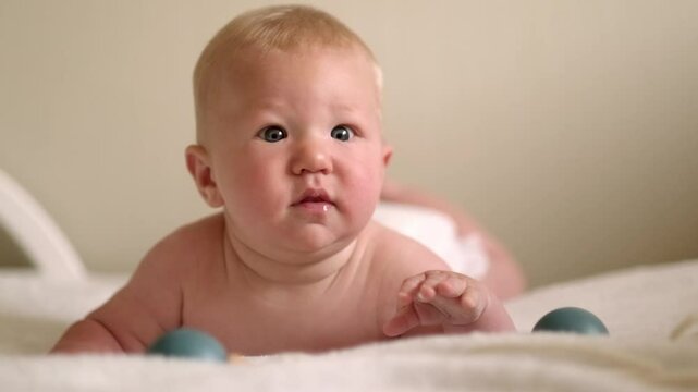 smiling infant baby lies on their tummy, looking up with bright eyes, Cild face expresses pure joy and curiosity, baby emotions, childhood happiness, home comfort