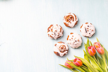 Cupcakes or muffins with icing and tulips on a light blue background. Easter cakes with chocolate chips. Space for text. View from above. Flat lay.