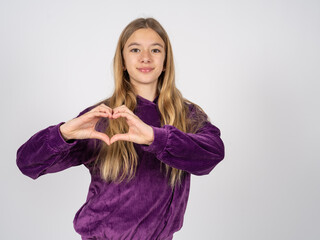 beautiful teen girl wearing purple sweater smiling in love doing heart symbol shape with hands. Romantic concept.