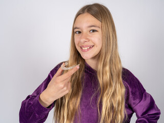 beautiful teen girl wearing purple sweater holding an invisible aligner ready to use it. Dental healthcare and confidence concept.