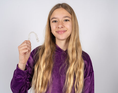 beautiful teen girl wearing purple sweater holding an invisible braces aligner, recommending this new treatment. Dental healthcare concept.