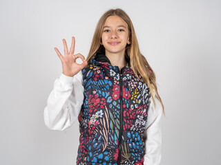 beautiful teen girl wearing colorful vest hold hand arm okey symbol toothy approve advising novelty...
