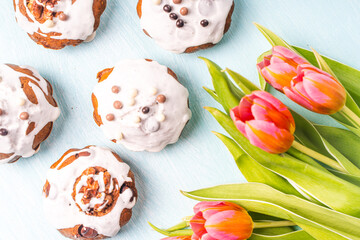 Cupcakes or muffins with icing and tulips on a light blue background. Easter cakes with chocolate chips. View from above. Flat lay.