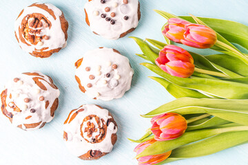 Cupcakes or muffins with icing and tulips on a light blue background. Easter cakes with chocolate chips. View from above. Flat lay.