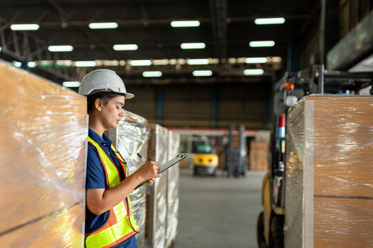 Worker conducts inventory check in warehouse with safety gear in bright industrial environment during daytime shift