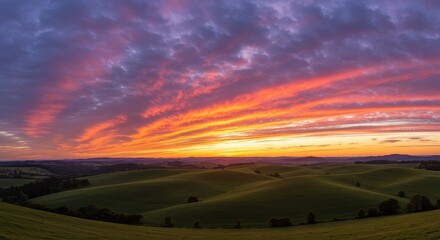 Obraz premium Vibrant sunset over rolling green hills with dramatic cloud formations