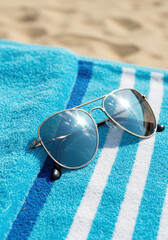 Aviator sunglasses resting on a blue and white striped towel evoke a carefree day at the beach.