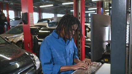Stationary computer with display. Male mechanic is with car in garage.