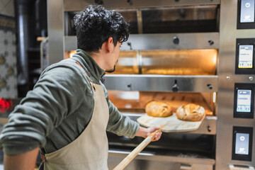 Baker taking freshly baked bread out of oven with wooden peel