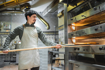 Baker putting bread in oven with wooden shovel in bakery