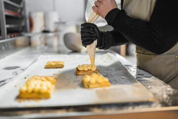 Pastry chef decorating pastries with cream using piping bag in bakery