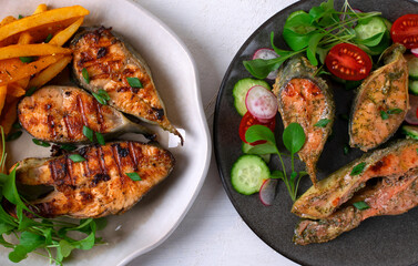 Oven baked pink salmon steaks with vegetable salad and fried pink salmon steaks with French fries and arugula on white background. Two dishes of healthy and unhealthy food