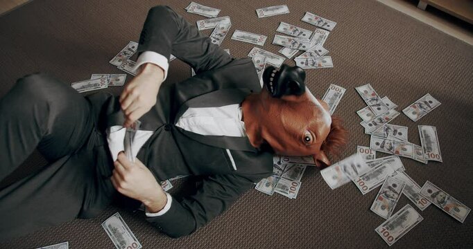 Businessman with horse mask counting stack cash money dollar profit salary wage earnings on workplace. Concept of salary or profit. Handsome happy businessman with horse mask scatters the dollars.