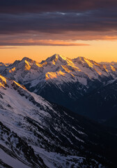 Snow capped mountain range bathed in golden sunrise light under a dramatic cloudy sky.