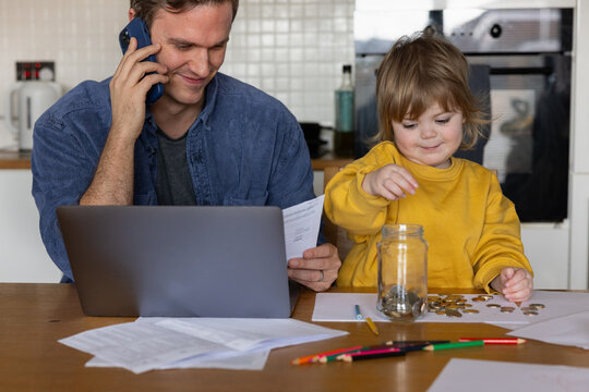 Child Counting Coins on the Table whilst her father pays bills