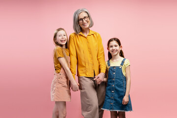 Grandmother holding hands with granddaughters smiling on pink background