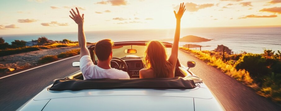 Young couple in a white convertible car on a coastal road, hands raised, happy and excited, with the sunset light behind them, viewed from the back - a summer vacation concept.