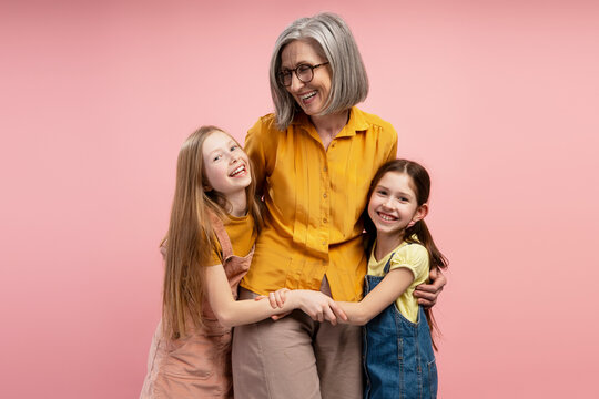 Grandmother embracing granddaughters celebrating Easter on pink background