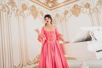Elegant woman in a pink baroque dress singing by a white piano