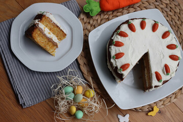 Sliced homemade carrot cake with mascarpone cream cheese icing and mini marzipan carrot decorations with Easter eggs and decorations