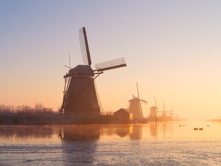 Windmills in the Netherlands during sunrise. Foggy morning and sunshine. Dutch canals. Photo for background, wallpaper, postcards.