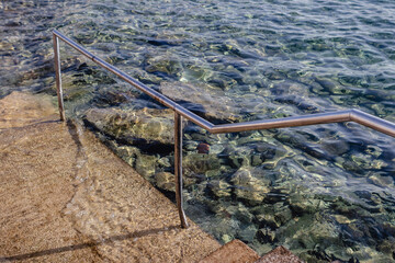 Stairs leading to the water, metal handrail, crystal-clear seawater