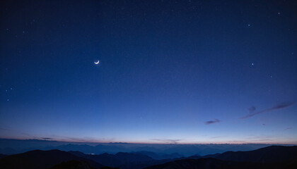 Starry night sky with crescent moon over majestic mountains, tranquility