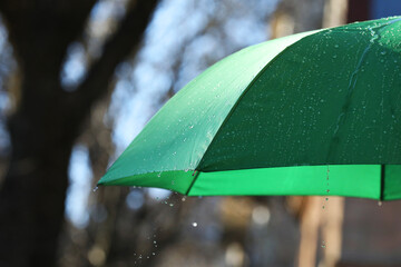 Open green umbrella under pouring rain outdoors, closeup