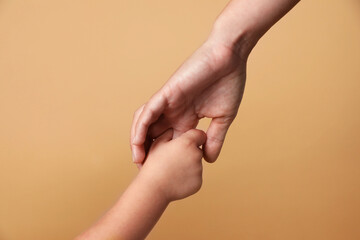 Mother and child holding hands on beige background, closeup