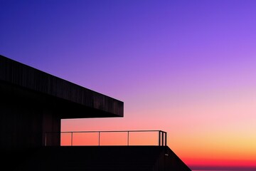 Obraz premium A modern building silhouette against a vibrant sunset backdrop, showcasing a gradient of purples and oranges in the sky.