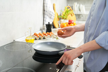 Woman breaking egg into frying pan in kitchen, closeup
