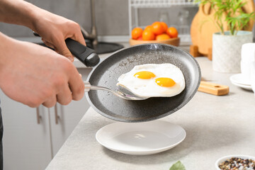 Man putting tasty fried eggs onto plate from frying pan in kitchen, closeup