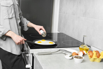 Woman adding salt into frying pan while cooking eggs on cooktop in kitchen, closeup