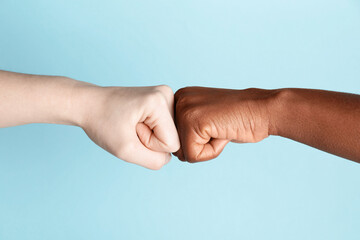 Stop racism. People of different skin colors bumping fists on light blue background, closeup