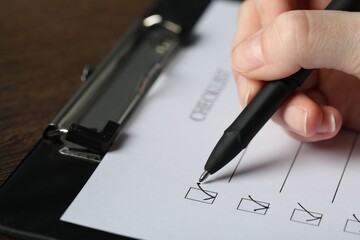 Woman filling Checklist with pen at table, closeup