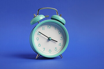 One turquoise alarm clock on blue background