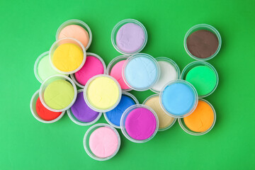 Different colorful modeling clay in plastic jars on green background, flat lay