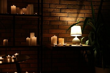 Many burning paraffin candles and glowing lamp in dark room
