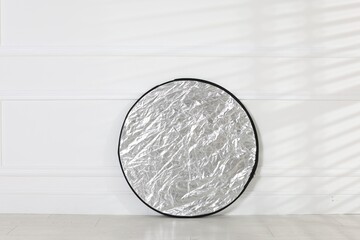 Professional reflector on floor near white wall. Photo studio equipment