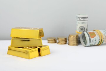 Shiny gold bars, dollar banknotes and coins on white table