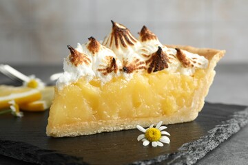 Piece of delicious pie with browned meringue and flowers on grey textured table, closeup