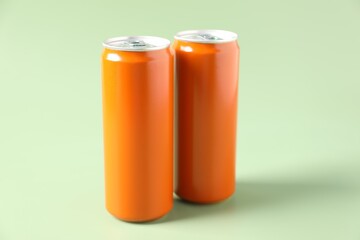 Orange aluminium cans of beverage on pale green background