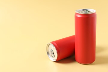 Red aluminium cans of beverage on pale yellow background, space for text