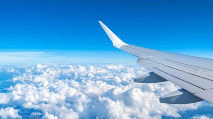 Fototapeta premium Airplane wing above fluffy clouds against a clear blue sky.